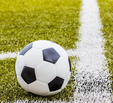 Classic black and white football placed on a green grass field near the touchline.