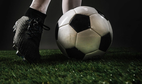 Close-up view of a football player standing beside a soccer ball on the field under dramatic lighting.